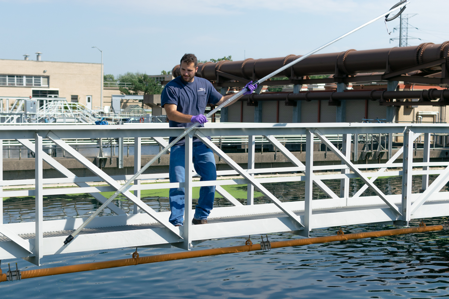 Photo of a Wastewater Treatment operator taking a water sample from a clarifier basin